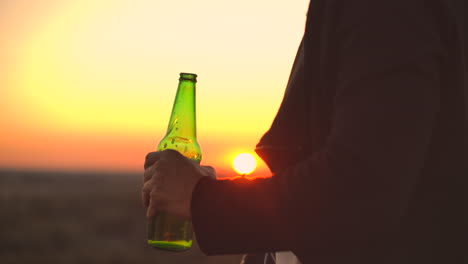 Close-up-of-a-man-drinking-beer-at-sunset-standing-on-the-roof-of-a-building-against-the-background-of-a-beautiful-evening-city.